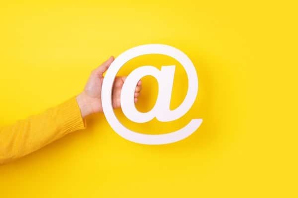 Die Hand einer Frau hält ein E-Mail-Symbol auf gelbem Hintergrund.