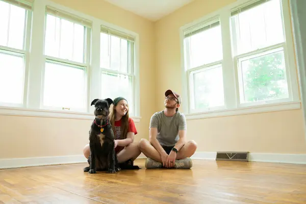 Ein Mann und eine Frau sitzen mit einem Hund auf dem Boden und diskutieren über die Webhosting-Auswahl.